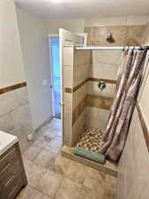 Full bath with a shower stall, vanity, and tile walls