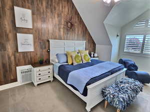 Carpeted bedroom featuring wooden walls and vaulted ceiling