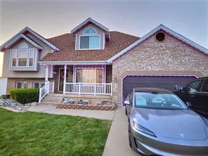 View of front facade featuring covered porch, a shingled roof, brick siding, a garage, and a front yard