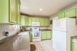 Kitchen featuring green cabinets, white appliances, recessed lighting, and dark countertops