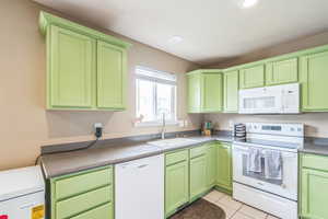 Kitchen featuring white appliances, green cabinetry, light tile patterned flooring, and recessed lighting