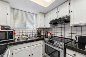 Kitchen featuring stainless steel appliances, white cabinets, backsplash, and under cabinet range hood