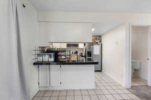 Kitchen featuring a peninsula, stainless steel fridge, light tile patterned flooring, white cabinets, and range hood