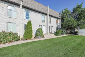 View of side of home featuring a shingled roof, mansard roof, a yard, and brick siding