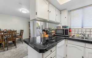 Kitchen featuring white cabinets, a peninsula, dishwasher, stainless steel microwave, and decorative backsplash