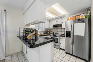 Kitchen with a peninsula, appliances with stainless steel finishes, white cabinetry, and decorative backsplash