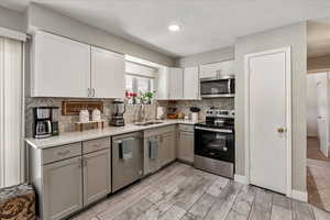 Kitchen featuring appliances with stainless steel finishes, decorative backsplash, light wood-style floors, white cabinets, and gray cabinetry