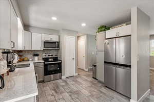 Kitchen with appliances with stainless steel finishes, tasteful backsplash, light wood-style floors, light stone countertops, and white cabinets
