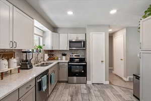Kitchen with appliances with stainless steel finishes, backsplash, light wood-style flooring, recessed lighting, and white cabinets