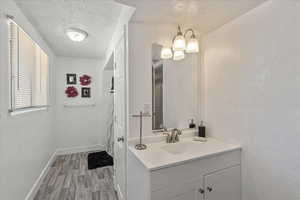 Bathroom featuring vanity, a textured ceiling, wood finished floors, and a textured wall