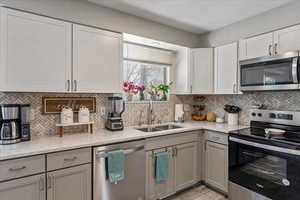 Kitchen featuring appliances with stainless steel finishes, decorative backsplash, light stone counters, and white cabinetry