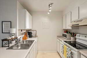 Kitchen with white appliances, under cabinet range hood, light countertops, and white cabinets