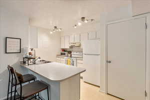 Kitchen featuring white appliances, a peninsula, a breakfast bar, white cabinetry, and light countertops