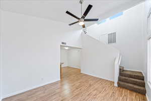 Unfurnished living room featuring light wood-style floors, stairway, a ceiling fan, and a towering ceiling