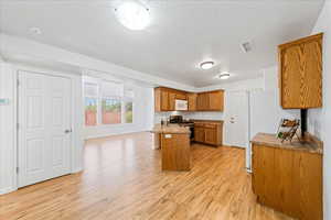 Kitchen featuring light wood-style floors, brown cabinets, white appliances, a textured ceiling, and a breakfast bar area
