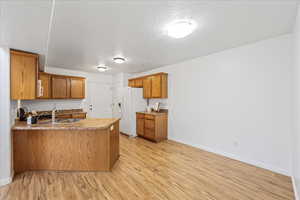 Kitchen featuring brown cabinetry, a peninsula, a textured ceiling, light wood-style floors, and white fridge with ice dispenser