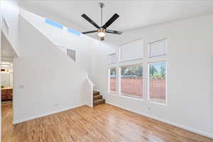 Unfurnished living room featuring stairway, a high ceiling, light wood-type flooring, and a ceiling fan