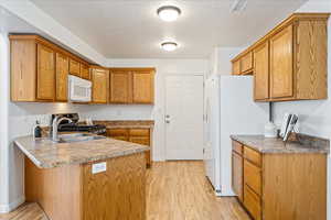 Kitchen with a peninsula, light wood-style flooring, white appliances, a textured ceiling, and brown cabinets