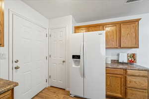 Kitchen with white fridge with ice dispenser, dark countertops, light wood-style floors, and brown cabinets