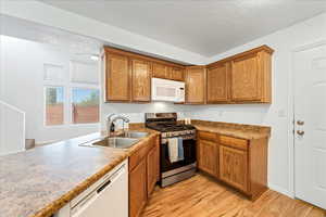 Kitchen featuring white appliances, brown cabinetry, light wood-style flooring, and a textured ceiling