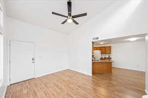 Unfurnished living room with high vaulted ceiling, a ceiling fan, and light wood-style floors