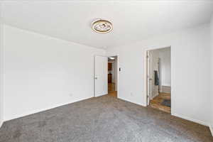 Unfurnished bedroom featuring carpet flooring, a textured ceiling, and ensuite bath