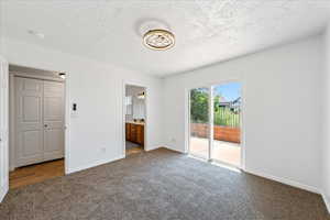 Unfurnished bedroom with carpet, access to outside, a textured ceiling, and connected bathroom