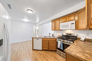 Kitchen featuring white appliances, brown cabinets, light wood finished floors, a textured ceiling, and a peninsula