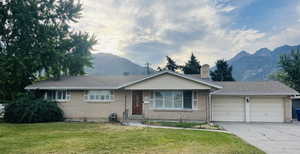 Single story home featuring brick siding, a mountain view, concrete driveway, a garage, and a front yard