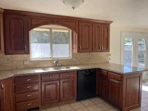 Kitchen featuring black dishwasher, a peninsula, decorative backsplash, and light stone counters