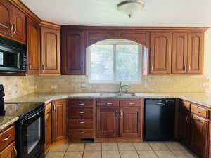 Kitchen with black appliances, light stone counters, tasteful backsplash, and light tile patterned floors