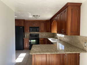 Kitchen featuring black appliances, a peninsula, light stone countertops, and backsplash