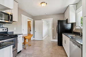 Kitchen with appliances with stainless steel finishes, white cabinetry, and dark stone countertops