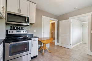 Kitchen featuring stainless steel appliances, white cabinets, and dark stone counters
