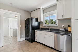 Kitchen featuring stainless steel dishwasher, black fridge, white cabinetry, and dark stone countertops