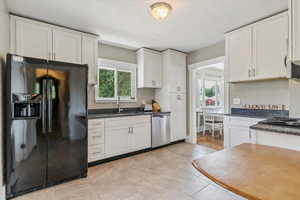 Kitchen with black fridge, white cabinetry, plenty of natural light, and dishwasher