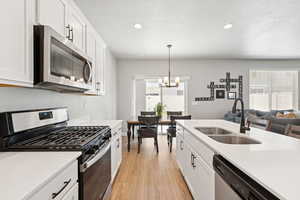 Kitchen with appliances with stainless steel finishes, a chandelier, light countertops, white cabinetry, and recessed lighting