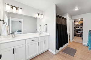 Bathroom with wood finished floors, double vanity, a spacious closet, a shower with shower curtain, and ensuite bath