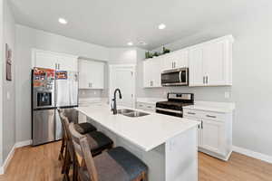 Kitchen featuring appliances with stainless steel finishes, light wood-style flooring, a breakfast bar, an island with sink, and white cabinets