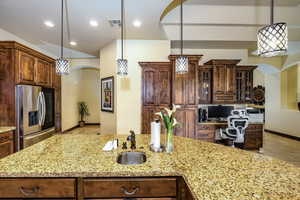 Kitchen featuring stainless steel refrigerator with ice dispenser, light stone counters, glass insert cabinets, arched walkways, and pendant lighting