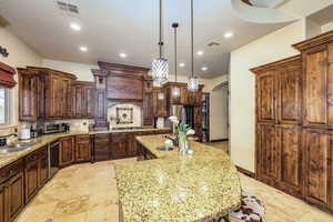 Kitchen featuring arched walkways, decorative backsplash, light stone counters, an island with sink, and hanging light fixtures