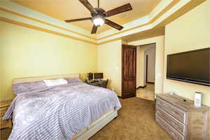 Bedroom with carpet, a raised ceiling, and a ceiling fan