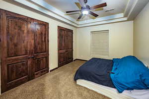 Carpeted bedroom featuring a tray ceiling and ceiling fan