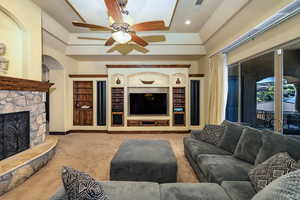Carpeted living room featuring a fireplace, built in shelves, ceiling fan, recessed lighting, and arched walkways
