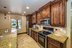 Kitchen with stainless steel appliances, recessed lighting, backsplash, decorative light fixtures, and light stone countertops