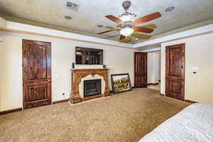 Bedroom featuring a tray ceiling, carpet floors, a high end fireplace, and a ceiling fan
