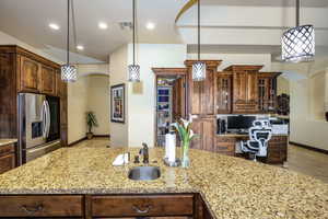 Kitchen featuring stainless steel fridge, light stone counters, glass insert cabinets, recessed lighting, and pendant lighting