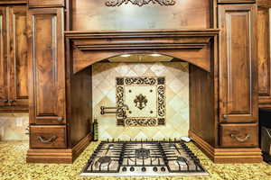 Detailed view of range hood, stainless steel gas stovetop, and tasteful backsplash