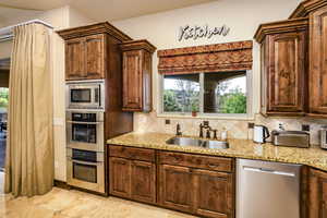 Kitchen with stainless steel appliances, light stone counters, and backsplash