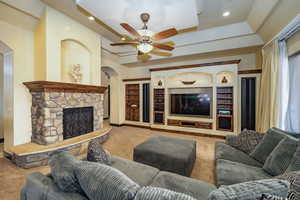 Carpeted living area featuring arched walkways, a fireplace, built in shelves, ceiling fan, and recessed lighting